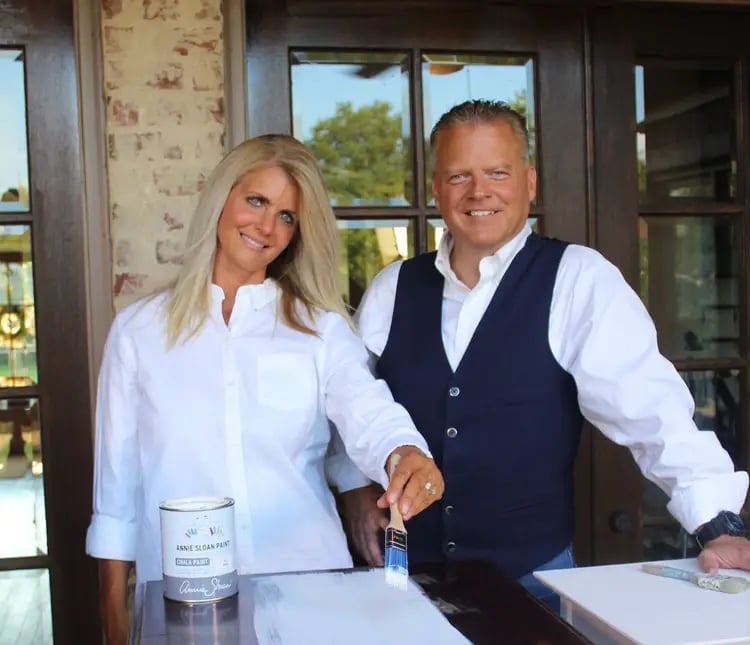 Two professionals smiling at a counter with wine bottles, in front of large windows and modern interior